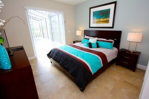 A bedroom with a bed, two bedside tables, a nightstand, a lamp, a picture on the wall, and a window with blinds.
