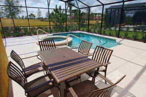 A poolside area with a wooden table and chairs, a hot tub, and a view of the surrounding landscape.