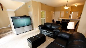 Una sala de estar con un televisor de pantalla plana grande, sofás de cuero negro, una mesa de centro y una escalera que conduce a otro nivel.