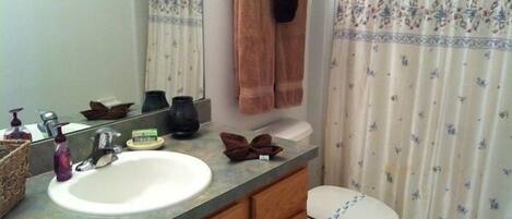 Un baño con lavamanos, espejo e inodoro. Hay toallas colgadas en la pared y una cortina de ducha con estampado floral.