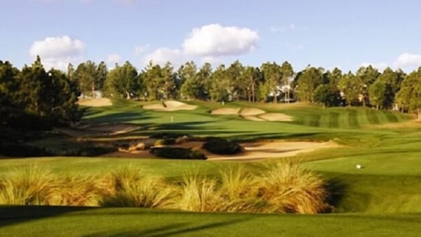 Un parcours de golf avec des bunkers de sable, un drapeau et un ciel dégagé.