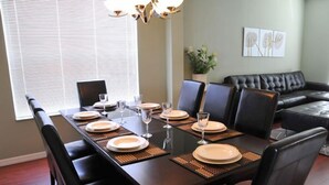 A dining area with a long table set for four, surrounded by black chairs. There is a black leather sofa in the background, and a small potted plant on the wall. - Ov3990 - Emerald Island - 7 Bed 4.5 Baths Villa (Kissimmee)