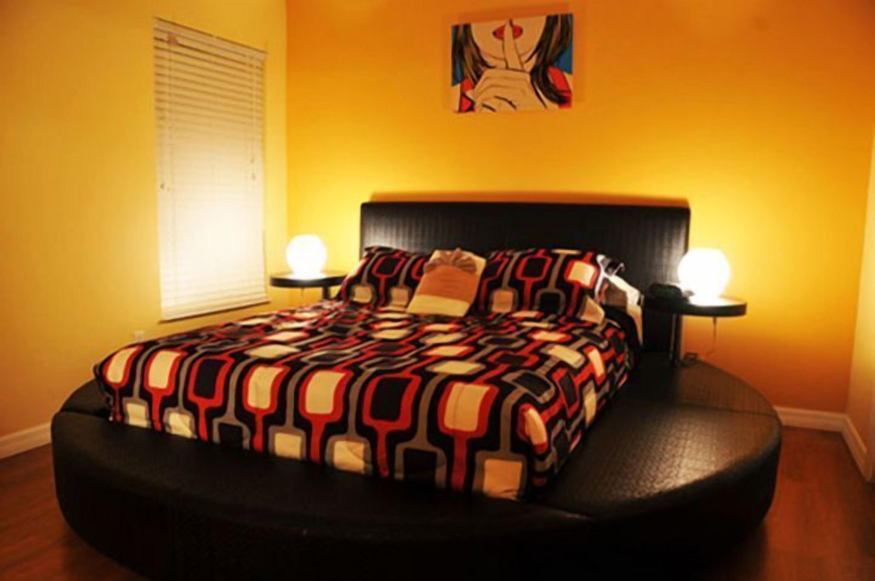 Uma cama com colcha estampada, duas luminárias de cabeceira e uma obra de arte na parede acima da cama.