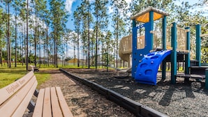 A playground with a slide and climbing structures, surrounded by a forested area and a bench. - Ov4075 - Highlands Reserve - 4 Bed 3 Baths Villa (Davenport)