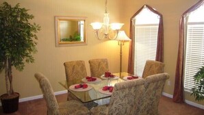 A dining area with a glass table, six patterned chairs, a chandelier, a mirror, and a potted plant. - Ov4075 - Highlands Reserve - 4 Bed 3 Baths Villa (Davenport)