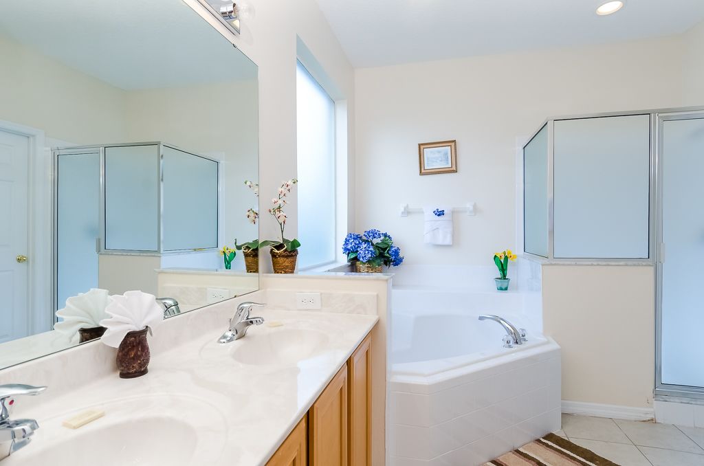A modern bathroom with a large mirror, two sinks, a bathtub, and decorative flowers.