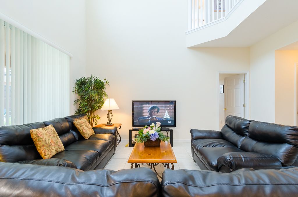 A living room with two black leather sofas, a wooden coffee table, a TV, and a potted plant.