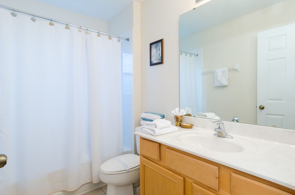A bathroom with a white shower curtain, a toilet, a sink with a mirror, and wooden cabinets.