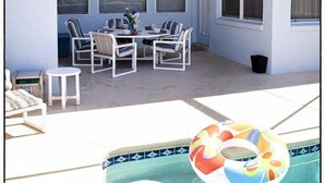 Um pátio externo com piscina, uma mesa de jantar com cadeiras e uma janela com cortinas.