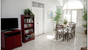 Uma sala de estar com televisão, estante de livros, mesa de jantar com cadeiras e um candelabro.