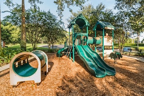 Explore a fun play area with a green slide, climbing structure, and tunnel amidst a serene natural setting.