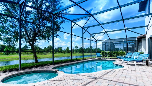 Une piscine dotée d’une enceinte en verre, entourée d’une terrasse en briques et de chaises longues à rayures bleues.
