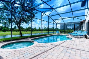 Uma piscina com cobertura de vidro, rodeada por um pátio de tijolos e espreguiçadeiras com listras azuis.