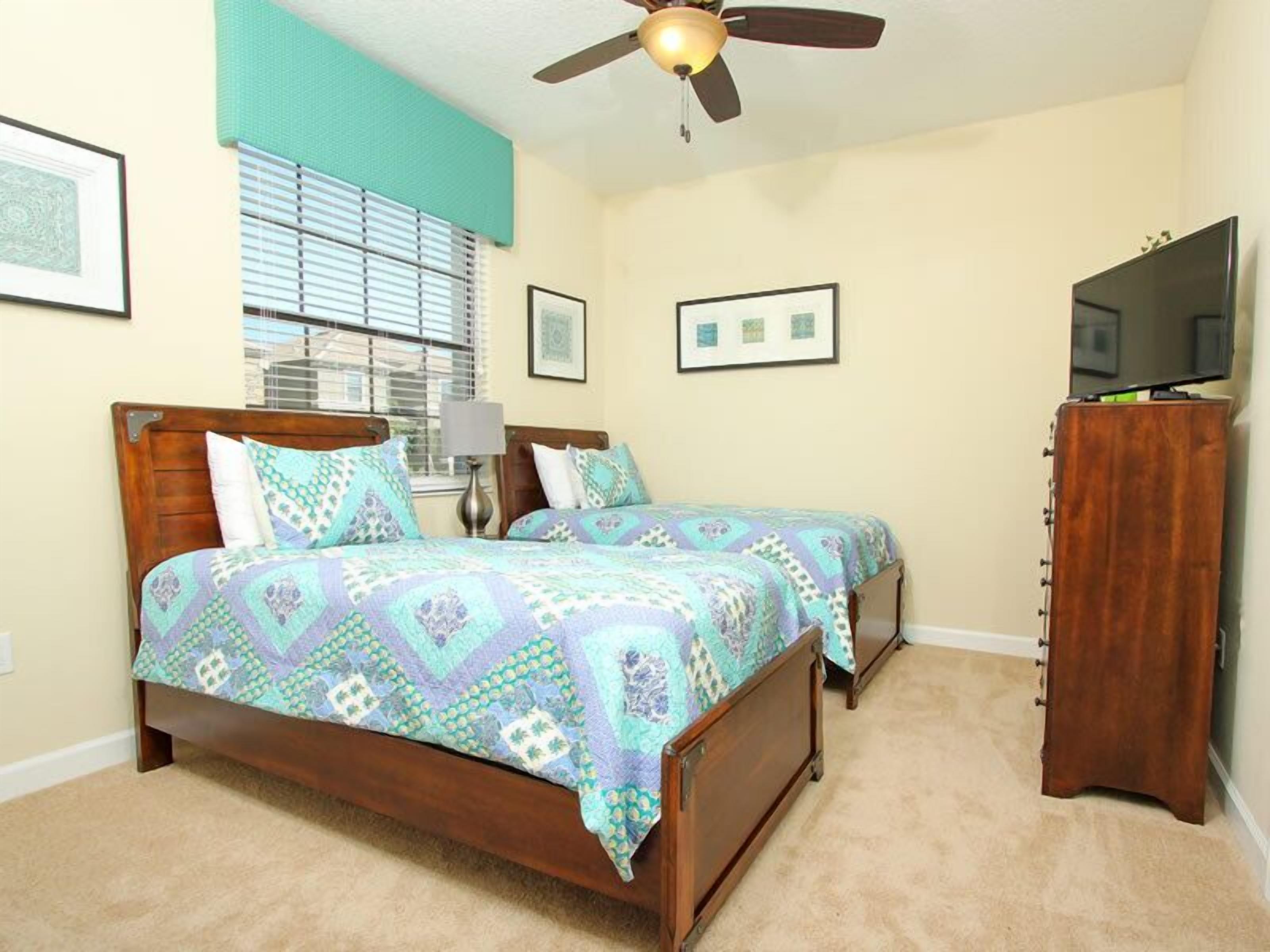 A bedroom with two beds, a ceiling fan, a TV, and a wooden cabinet.