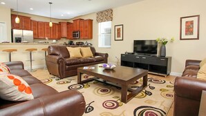 A living room with a brown leather sofa, a coffee table, and a TV stand. There is a kitchen in the background with wooden cabinets and a microwave. - Ov3851 - Champions Gate Resort - 4 Bed 3 Baths Townhome (Davenport)