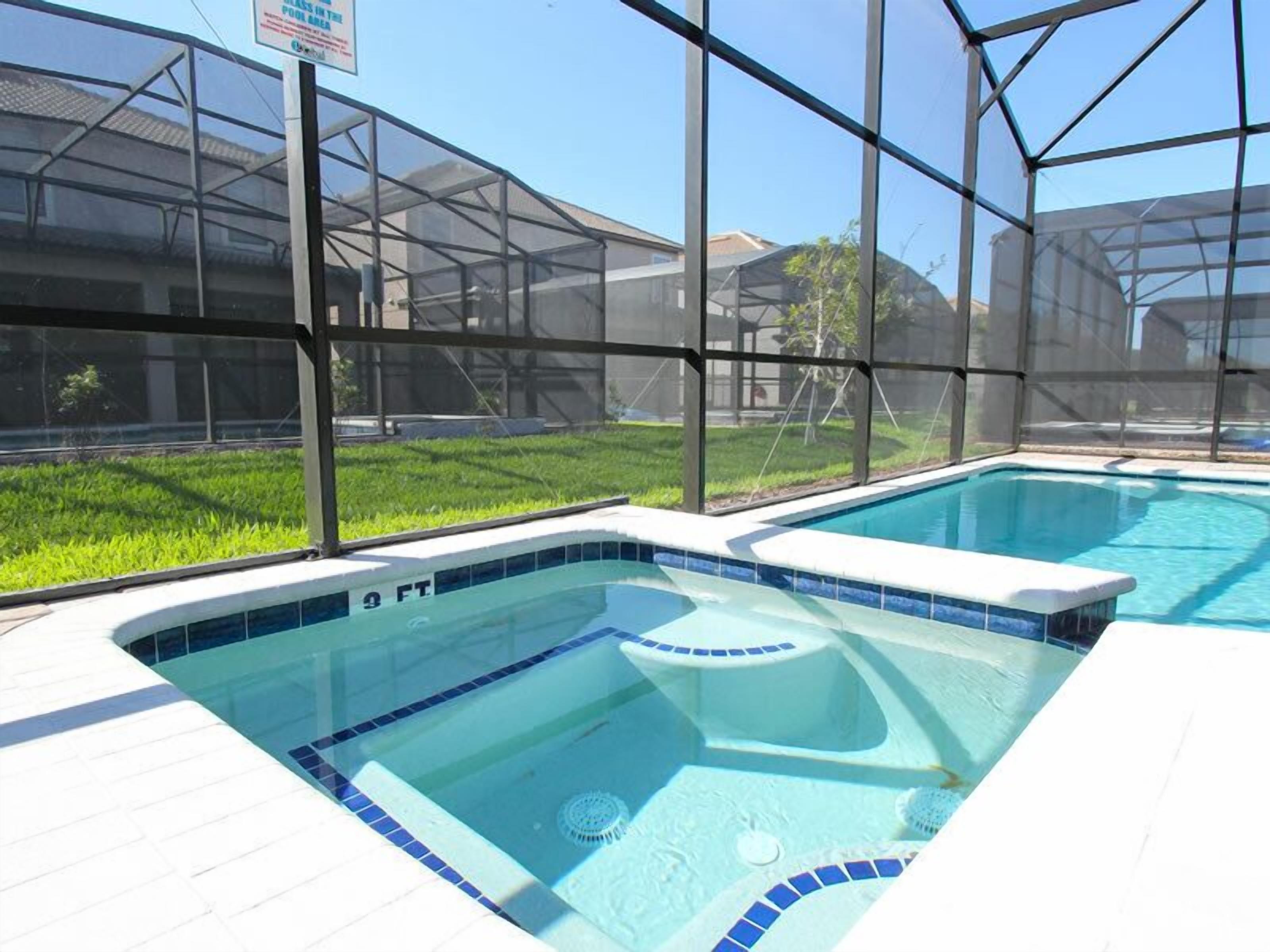 Ein Swimmingpool mit einer Tiefenmarkierung von 2,75 Metern, umgeben von einer Glaskonstruktion mit Blick auf eine Rasenfläche und Gebäude im Hintergrund.
