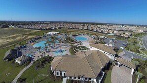 An aerial view of a residential area with multiple houses, a swimming pool complex, and a road. - Ov3851 - Champions Gate Resort - 4 Bed 3 Baths Townhome (Davenport)