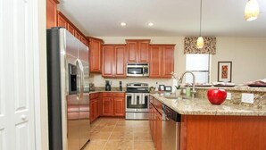 A modern kitchen with wooden cabinets, stainless steel appliances, and a granite countertop. - Ov3851 - Champions Gate Resort - 4 Bed 3 Baths Townhome (Davenport)