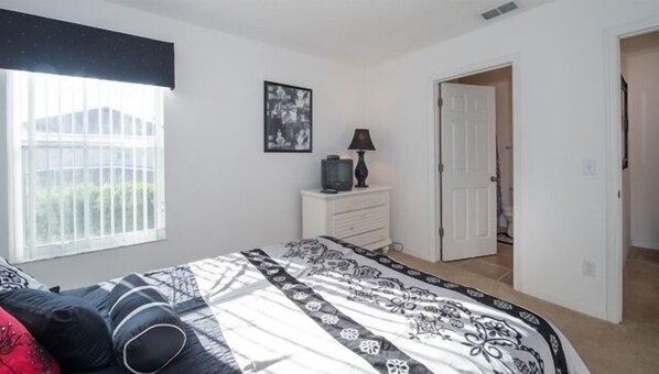 A bedroom with a bed, a dresser, a television, and a door leading to another room.