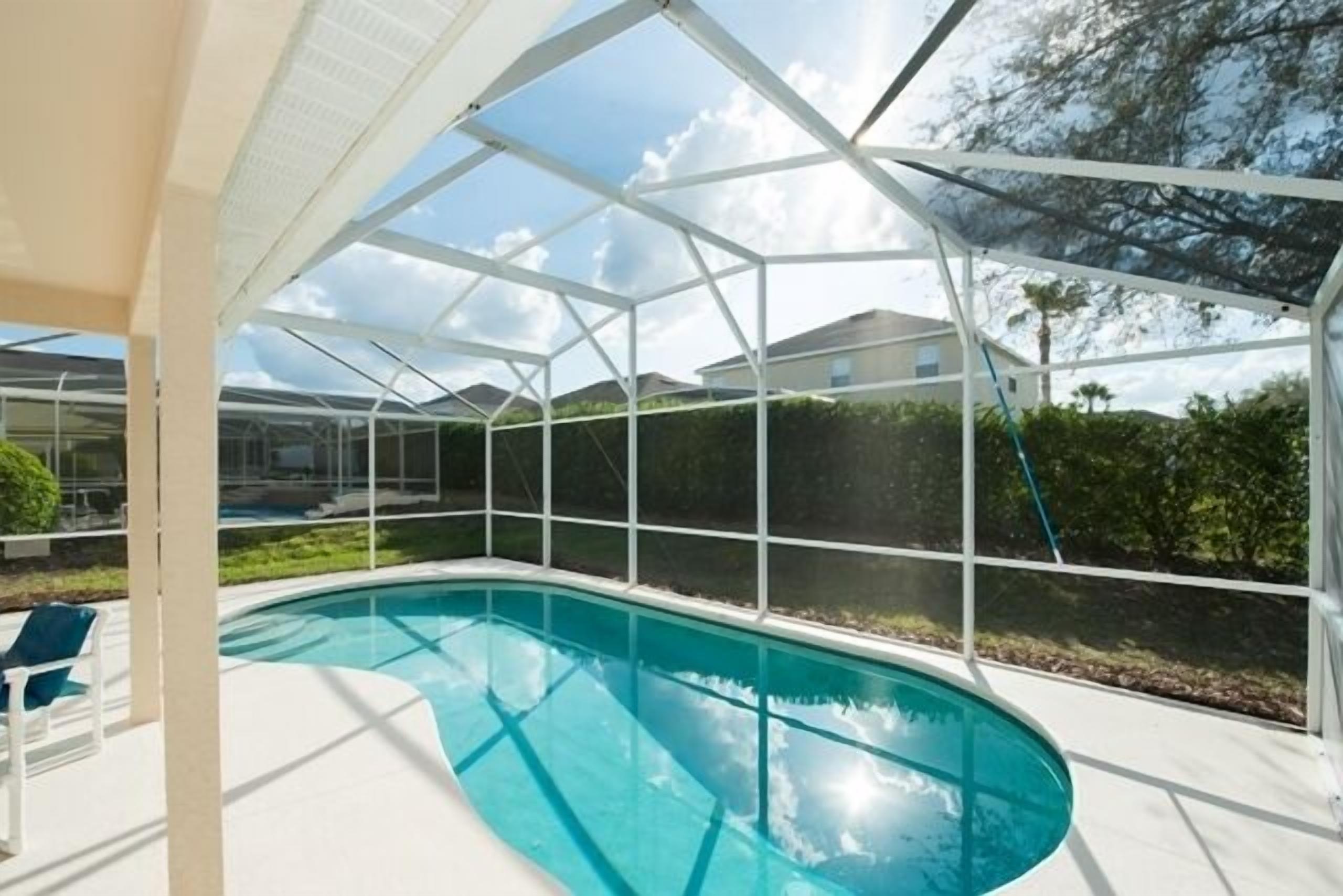 Ein Schwimmbad mit Glasveranda, umgeben von einer weißen Terrasse und Blick auf Häuser im Hintergrund.
