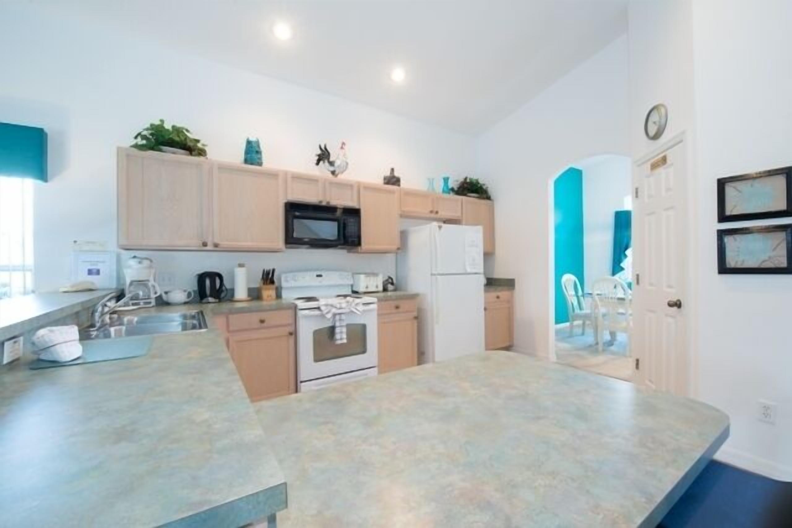 A modern kitchen with light wood cabinets, a microwave, a stove, and a refrigerator. There is a sink and a countertop with various items.