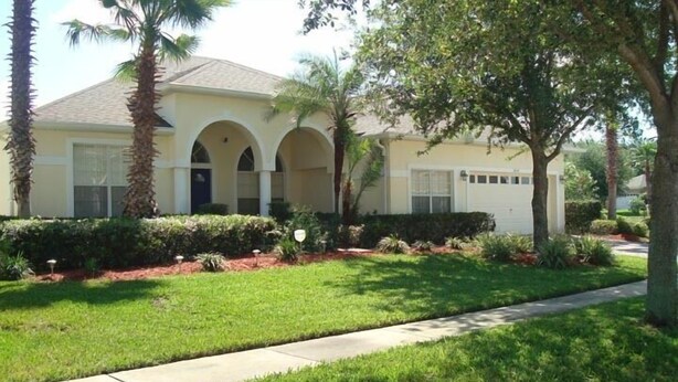 A single-story house with a light yellow facade, a covered patio with arches, and a well-maintained lawn.
