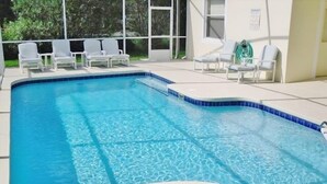 A swimming pool with a tiled edge, surrounded by white lounge chairs.