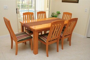 Un comedor con una mesa de madera y seis sillas, un mantel tejido y una planta en maceta.