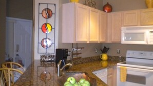 A kitchen with a granite countertop, a sink with a bowl of apples, a coffee maker, and a microwave. - Ov2568 - Emerald Island - 3 Bed 2.5 Baths Townhome (Kissimmee)