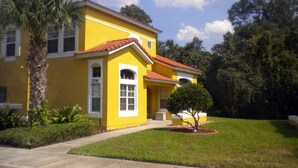 A yellow house with a red roof, surrounded by a well-maintained lawn and trees. - Ov2568 - Emerald Island - 3 Bed 2.5 Baths Townhome (Kissimmee)