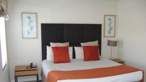 Ein Hotelzimmer mit einem großen Bett, einem Nachttisch mit Telefon, einer Lampe und gerahmten Kunstwerken an den Wänden.