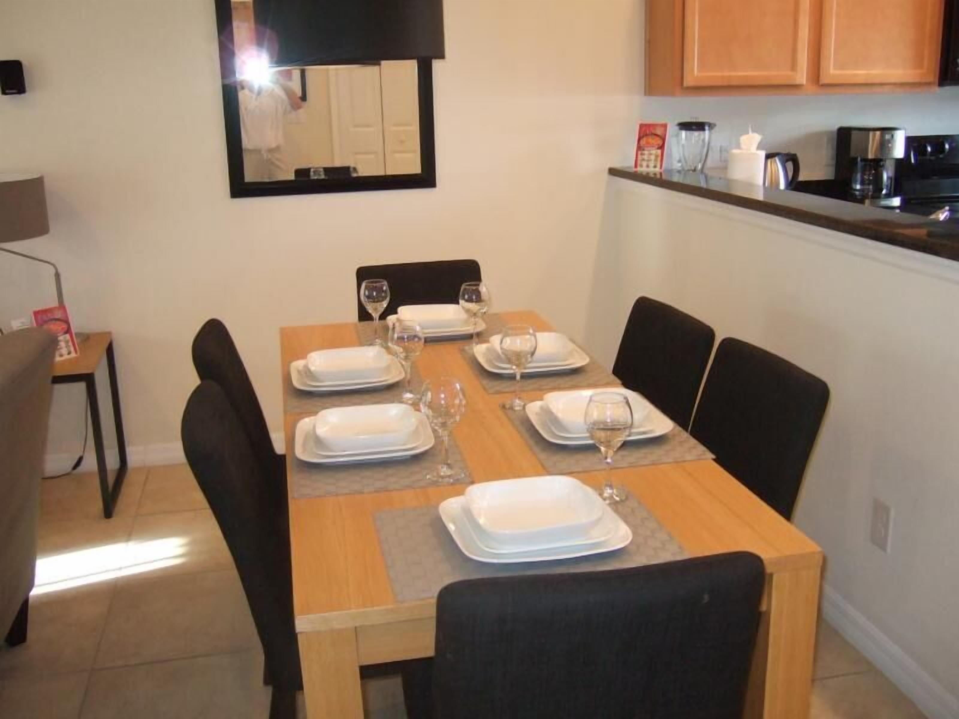 A dining area with a wooden table set for six, surrounded by black chairs.