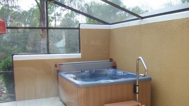 Ein kleiner, abgeschlossener Whirlpoolbereich mit einem Holzstufenaufgang, einem Metallarmaturen und Blick auf Grün hinter einem Fenster.