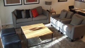 Ein Wohnzimmer mit grauem Sofa, einem Holztisch und einem grauen Sessel. An der Wand hängen zwei gerahmte abstrakte Gemälde.