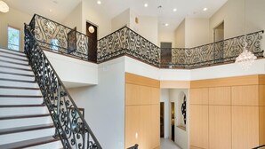 A multi-level interior with a staircase featuring ornate black railings, wooden flooring, and a chandelier. - Ov3978 - Formosa Gardens - 7 Bed 7.5 Baths Villa (Kissimmee)
