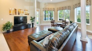 A spacious living room with a large leather sofa, a flat-screen TV, and a dining area with chairs and a table. - Ov3978 - Formosa Gardens - 7 Bed 7.5 Baths Villa (Kissimmee)