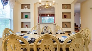 Ein Esszimmer mit gedecktem Tisch für sechs Personen, umgeben von verzierten Stühlen, einer Kandelaber und dekorativen Regalen mit Gegenständen.