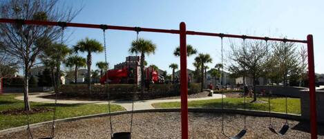 Un parque infantil con columpios y un tobogán rojo.