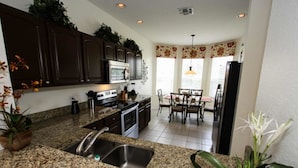 A kitchen with granite countertops, dark cabinets, a built-in oven, and a dining area with a table and chairs. - Ov4195 - Windsor Hills Resort - 5 Bed 5 Baths Villa (Kissimmee)