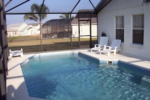 A swimming pool with clear blue water, surrounded by a covered patio area with white chairs.