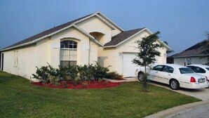 Einbungalow mit Garage, einem kleinen Vorgarten mit roter Rindenmulch und einem Baum.