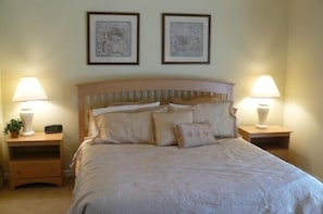 A neatly made bed with a wooden headboard, two bedside tables with lamps, and two framed pictures on the wall.