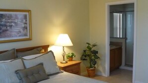 Ein Schlafzimmer mit Bett, Nachttischlampe, Blumentopf und einem Bild an der Wand.