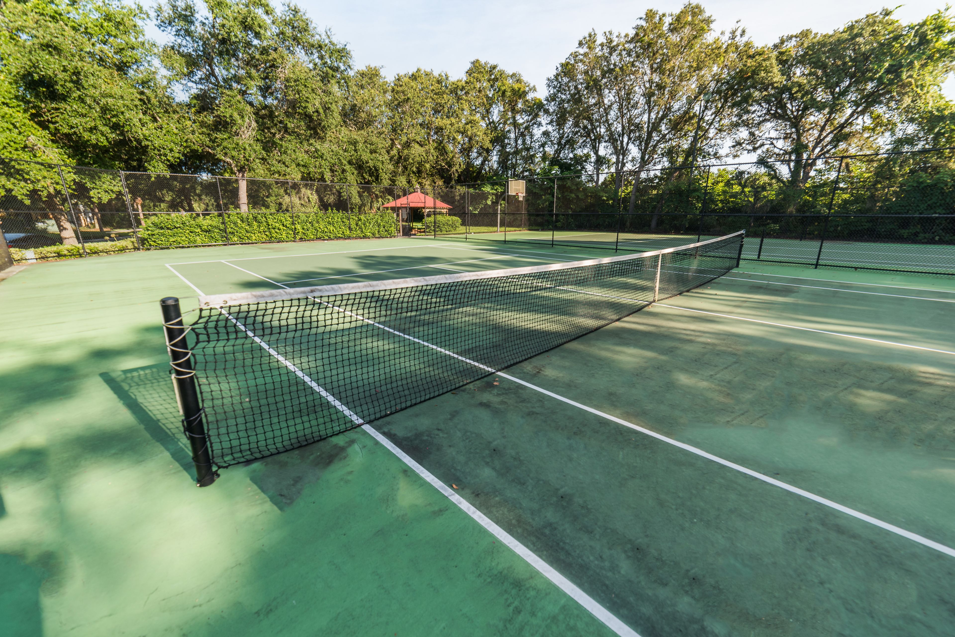 Cancha de tenis con red, rodeada de árboles y un pequeño pabellón.