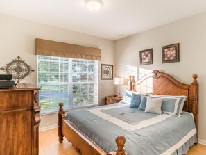 Un dormitorio con cama de madera, mesita de noche, cómoda y ventana con persianas.