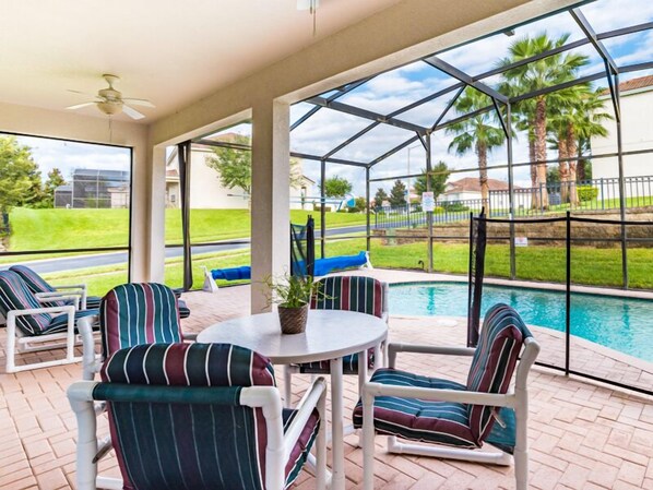 Un espacio exterior techado con piscina, sillones de descanso y una mesa.