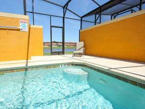 Une piscine à l’eau claire, un panneau indiquant les règles d’utilisation de la piscine, et une vue sur une étendue d’eau à travers de grandes fenêtres.