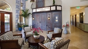 Un hall con un cartel que dice "Paradise Palms Cinema", con un balcón con plantas, sillas estampadas y ventiladores de techo.