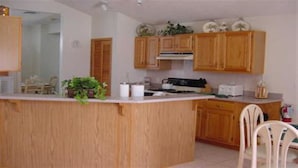 A kitchen with wooden cabinets, a white countertop, and a small island. There is a chair and a plant on the countertop. - Ov64 - Oak Island Harbour - 3 Bed 2.5 Baths Villa (Kissimmee)