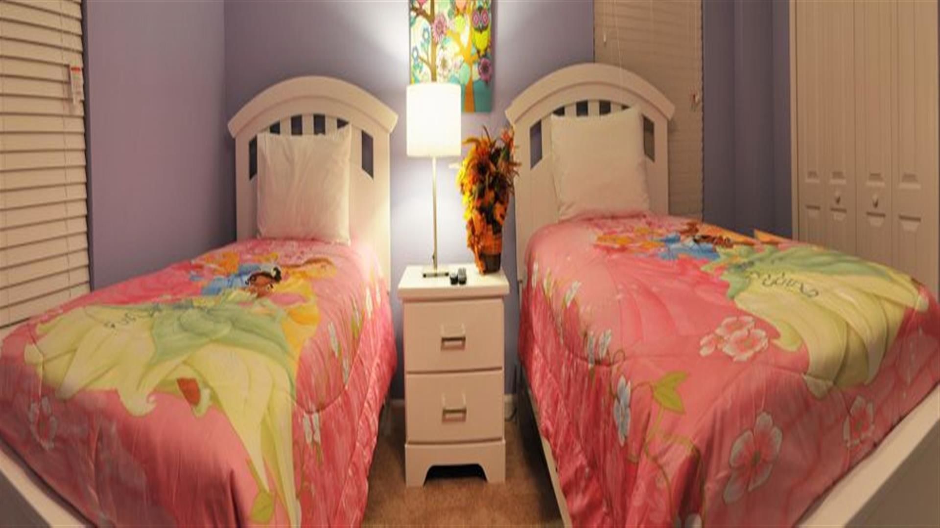 A bedroom with two single beds, a nightstand with drawers, a lamp, and a floral painting on the wall.